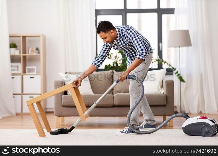 household and cleaning concept - indian man with vacuum cleaner at home. indian man with vacuum cleaner at home