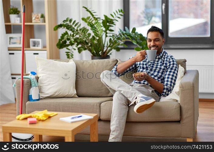 household and people concept - indian man drinking coffee and resting after home cleaning. indian man drinking coffee after home cleaning