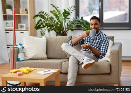 household and people concept - indian man drinking coffee and resting after home cleaning. indian man drinking coffee after home cleaning