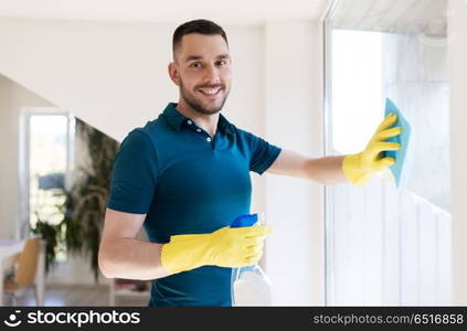 household and people concept - man in rubber gloves cleaning window with rag and spray cleaner at home. man in rubber gloves cleaning window with rag. man in rubber gloves cleaning window with rag