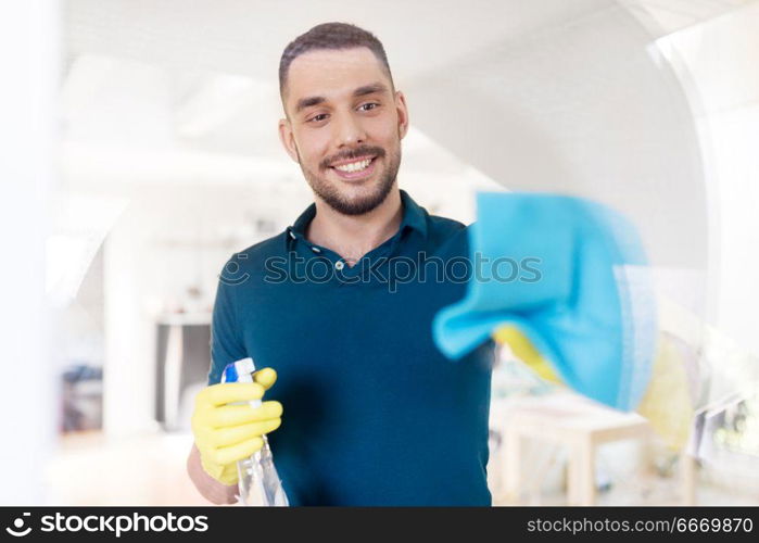 household and people concept - man in rubber gloves cleaning window with rag and spray cleaner at home. man in rubber gloves cleaning window with rag. man in rubber gloves cleaning window with rag