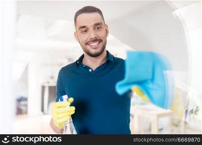 household and people concept - man in rubber gloves cleaning window with rag and spray cleaner at home. man in rubber gloves cleaning window with rag. man in rubber gloves cleaning window with rag
