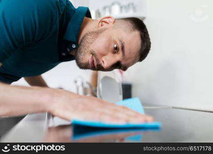 household and people concept - man wiping table with cloth cleaning cooker at home kitchen. man with rag cleaning cooker at home kitchen. man with rag cleaning cooker at home kitchen
