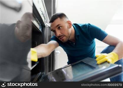 household and people concept - man wiping table with cloth cleaning inside oven at home kitchen. man with rag cleaning inside oven at home kitchen. man with rag cleaning inside oven at home kitchen