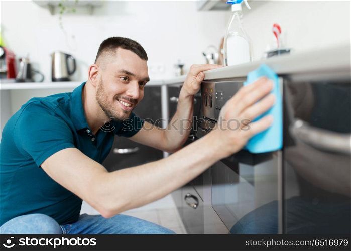 household and people concept - man wiping table with cloth cleaning oven door at home kitchen. man with rag cleaning oven door at home kitchen. man with rag cleaning oven door at home kitchen