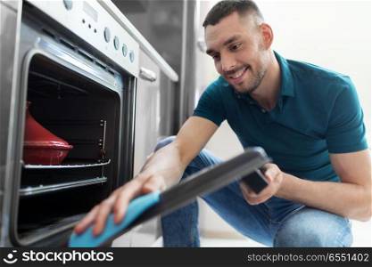household and people concept - man wiping table with cloth cleaning oven door at home kitchen. man with rag cleaning oven door at home kitchen. man with rag cleaning oven door at home kitchen