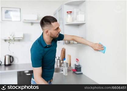 household and people concept - man with cloth cleaning wall at home kitchen. man with rag cleaning wall at home kitchen