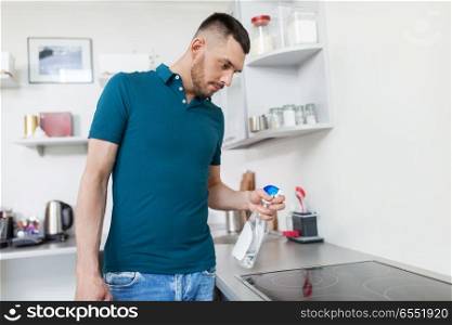 household and people concept - man with spray cleaner cleaning cooker at home kitchen. man with spray cleaning cooker at home kitchen. man with spray cleaning cooker at home kitchen