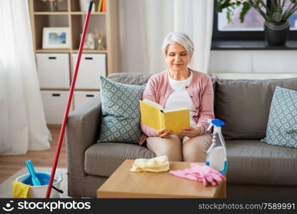 household and people concept - senior woman reading book and resting after home cleaning. senior woman reading book after home cleaning