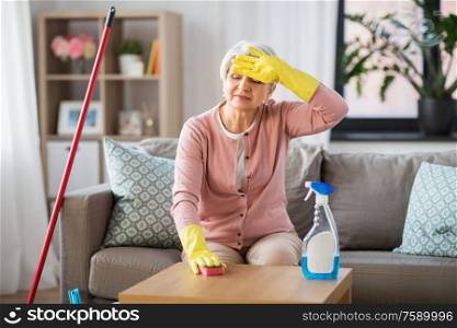 household and people concept - tired senior woman with detergent and sponge cleaning table at home. tired senior woman cleaning table at home