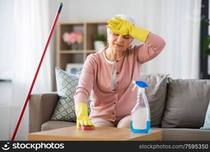 household and people concept - tired senior woman with detergent and sponge cleaning table at home. tired senior woman cleaning table at home