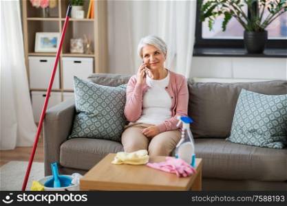 household and technology concept - happy senior woman calling on smartphone after cleaning home. old woman calling on cellphone after cleaning home