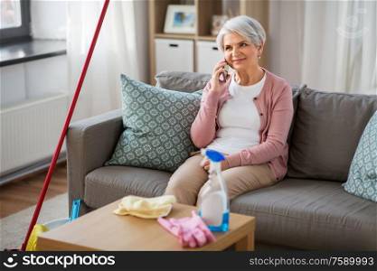 household and technology concept - happy senior woman calling on smartphone after cleaning home. old woman calling on cellphone after cleaning home