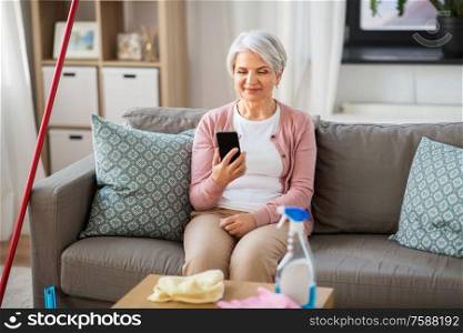 household and technology concept - happy senior woman using smartphone after cleaning home. senior woman using smartphone after cleaning home