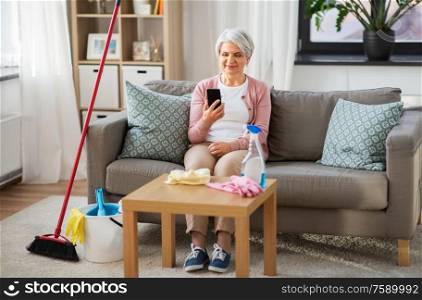 household and technology concept - happy senior woman using smartphone after cleaning home. senior woman using smartphone after cleaning home