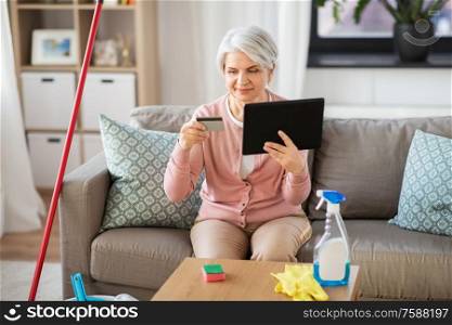 household and technology concept - happy senior woman with tablet pc computer and credit card after cleaning home. old woman with tablet pc and credit card at home
