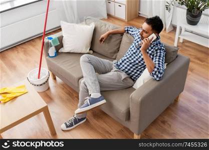 household and technology concept - indian man calling on smartphone after cleaning home. man calling on smartphone after cleaning home
