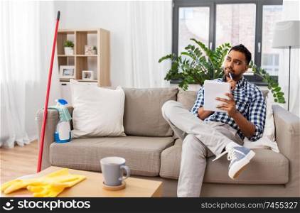 household and time management concept - indian man making to do list in notebook after home cleaning. indian man with to do list after home cleaning