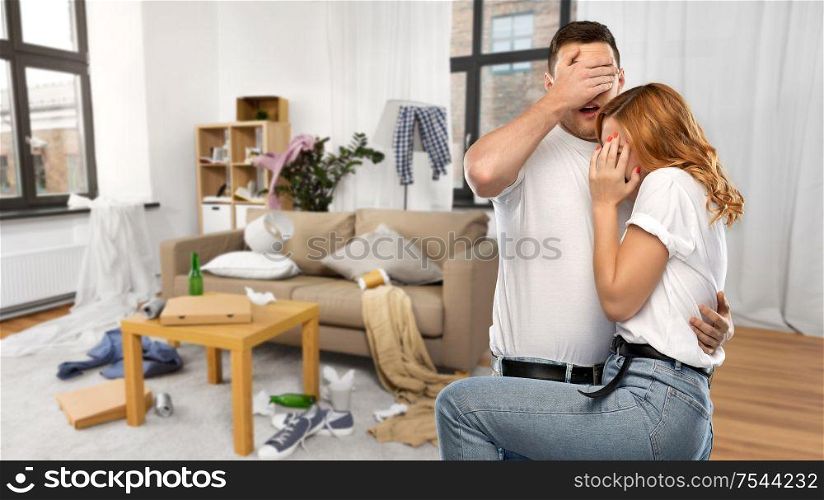 household, cleaning and domestic life concept - scared couple in white t-shirts over messy home room background. scared couple over messy home room