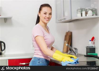 household, cleaning and people concept - happy woman or housewife in rubber gloves wiping table with microfiber cloth at home kitchen. woman or housewife cleaning table at home kitchen. woman or housewife cleaning table at home kitchen