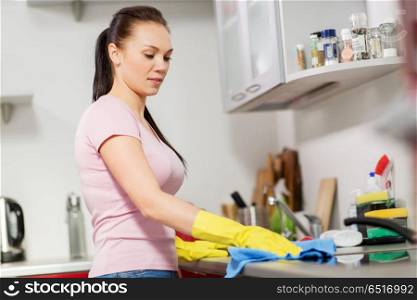 household, cleaning and people concept - happy woman or housewife in rubber gloves wiping table with microfiber cloth at home kitchen. woman or housewife cleaning table at home kitchen. woman or housewife cleaning table at home kitchen
