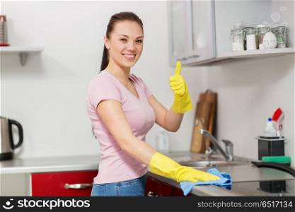 household, cleaning and people concept - happy woman or housewife in rubber gloves wiping table with microfiber cloth at home kitchen and showing thumbs up. woman or housewife cleaning table at home kitchen. woman or housewife cleaning table at home kitchen