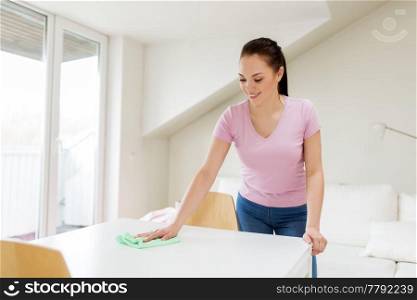 household, cleaning and people concept - happy woman or housewife wiping table with microfiber cloth at home. woman cleaning table with microfiber cloth at home