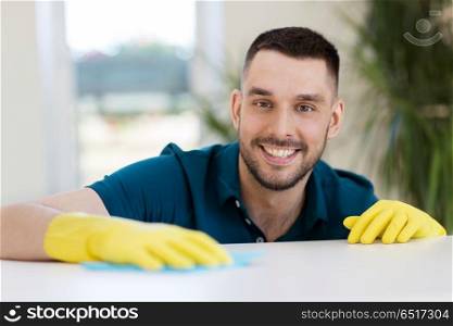 household, cleaning and people concept - smiling man wiping table with cloth at home. smiling man cleaning table with cloth at home. smiling man cleaning table with cloth at home