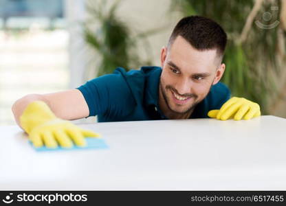 household, cleaning and people concept - smiling man wiping table with cloth at home. smiling man cleaning table with cloth at home. smiling man cleaning table with cloth at home