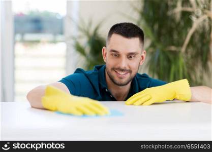 household, cleaning and people concept - smiling man wiping table with cloth at home. smiling man cleaning table with cloth at home. smiling man cleaning table with cloth at home