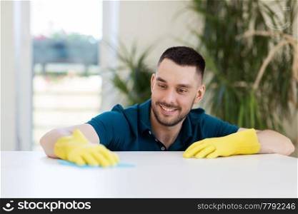 household, cleaning and people concept - smiling man wiping table with cloth at home. smiling man cleaning table with cloth at home