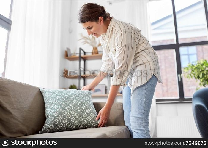 household, home improvement and cleaning concept - happy smiling woman arranging cushions on armchair and sofa. woman arranging cushions at home