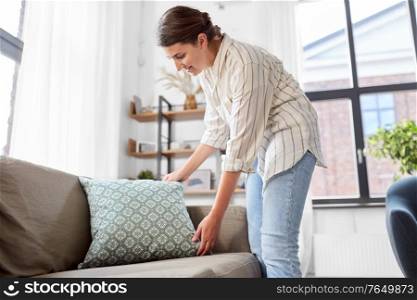 household, home improvement and cleaning concept - happy smiling woman arranging cushions on armchair and sofa. woman arranging cushions at home