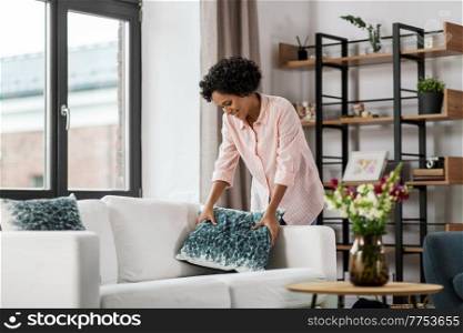 household, home improvement and cleaning concept - happy smiling young woman arranging cushions on sofa and sofa. happy woman arranging cushions on sofa at home