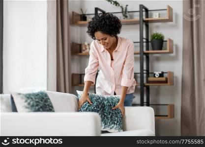 household, home improvement and cleaning concept - happy smiling young woman arranging cushions on sofa. happy woman arranging cushions on sofa at home