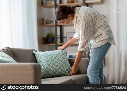 household, home improvement and cleaning concept - happy woman arranging cushions on armchair and sofa. happy woman arranging cushions at home
