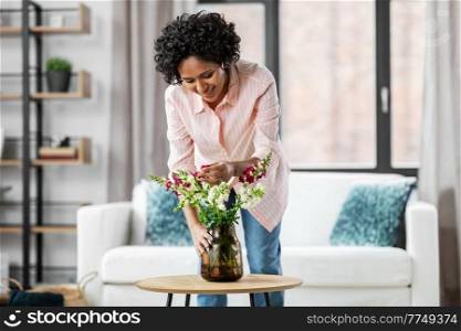 household, home improvement and interior concept - happy smiling young woman placing flowers on coffee table. happy woman placing flowers on table at home