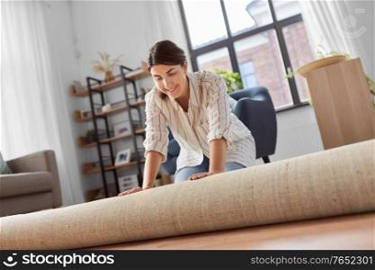 household, home improvement and interior concept - happy smiling young woman unfolding carpet. young woman unfolding carpet at home