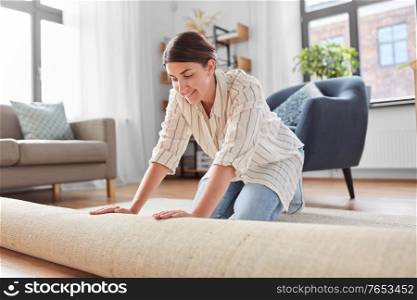 household, home improvement and interior concept - happy smiling young woman unfolding carpet. young woman unfolding carpet at home