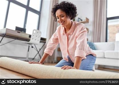 household, home improvement and interior concept - happy smiling young woman unfolding carpet on floor. young woman unfolding carpet at home