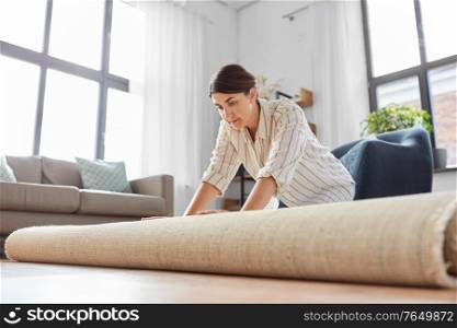 household, home improvement and interior concept - young woman unfolding carpet. young woman unfolding carpet at home