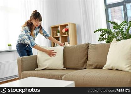 household, housework and cleaning concept - asian woman arranging sofa cushions at home. asian woman arranging sofa cushions at home