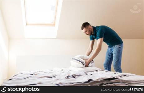 household, housework and cleaning concept - happy man making bed at home. happy man making bed at home. happy man making bed at home