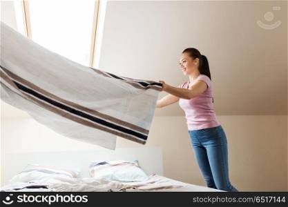 household, housework and cleaning concept - happy woman or housewife with towel making bed at home. happy woman or housewife making bed at home. happy woman or housewife making bed at home