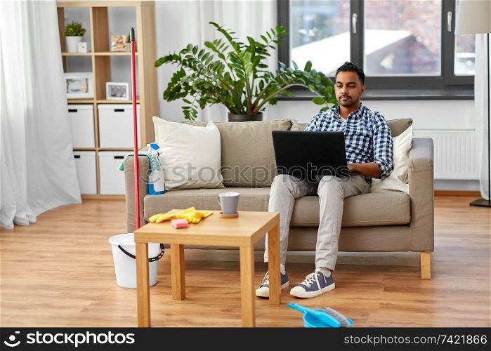 household, housework and technology concept - indian man with laptop computer, mop and bucket after home cleaning. man with laptop computer after home cleaning