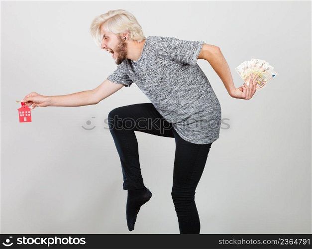 Household savings and finances, economy concept. Happy running man holding money and keys to house, studio shot on grey background. Man holding money and keys to house