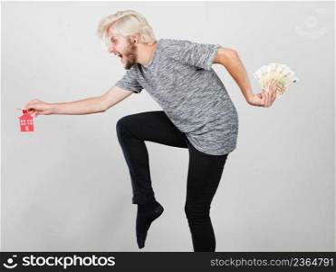 Household savings and finances, economy concept. Happy running man holding money and keys to house, studio shot on grey background. Man holding money and keys to house