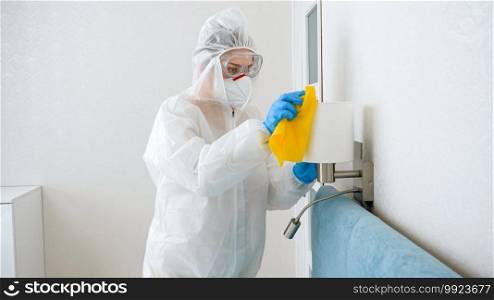 Housekeeper or maid cleaning and desinfecting furniture in hotel room. Person wearing protective medical suit doing cleanup at home.. Housekeeper or maid cleaning and desinfecting furniture in hotel room. Person wearing protective medical suit doing cleanup at home
