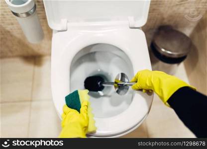 Housemaid hands in rubber gloves cleans the toilet with brush, hotel restroom interior on background. Professional housekeeping service, charwoman, sanitary processing