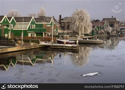 Houses and a riped tree along the covered with floating ice river Zaan. Houses along the river Zaan
